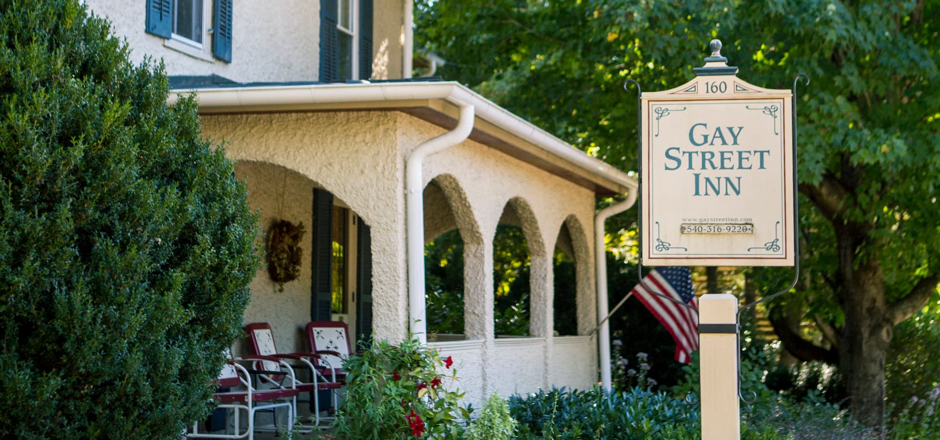 A quaint inn sign stands in front of a charming house surrounded by greenery.