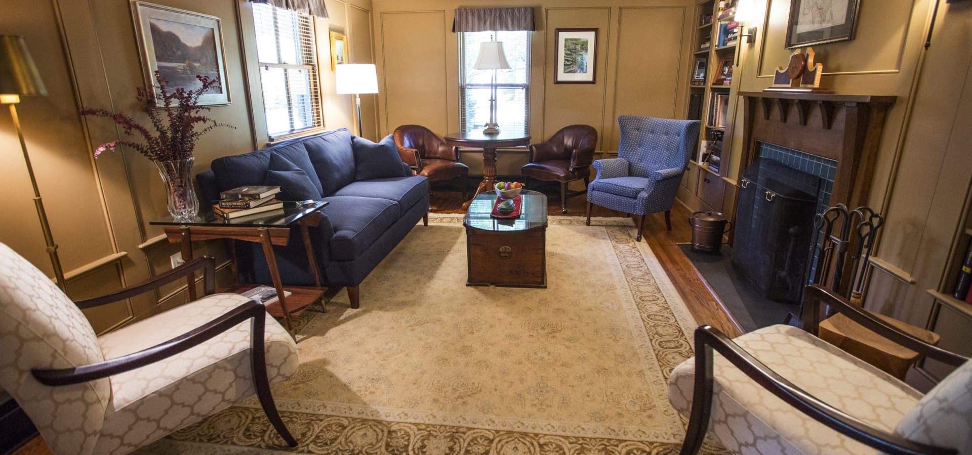 A cozy living room featuring a blue sofa, armchairs, a coffee table, and a fireplace.