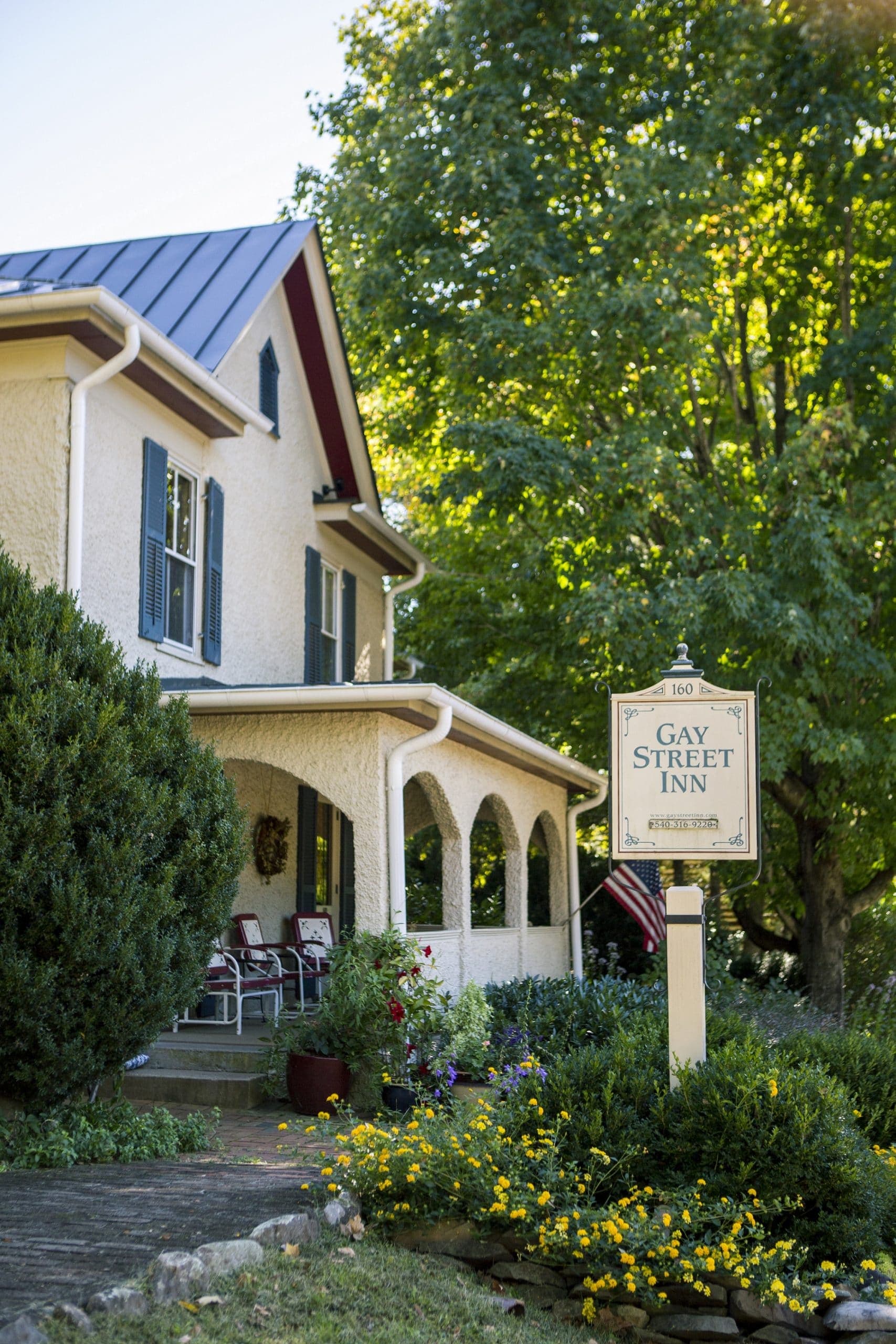 A two story stucco house with a large porch with arches and a sign in front that says Gay Street Inn