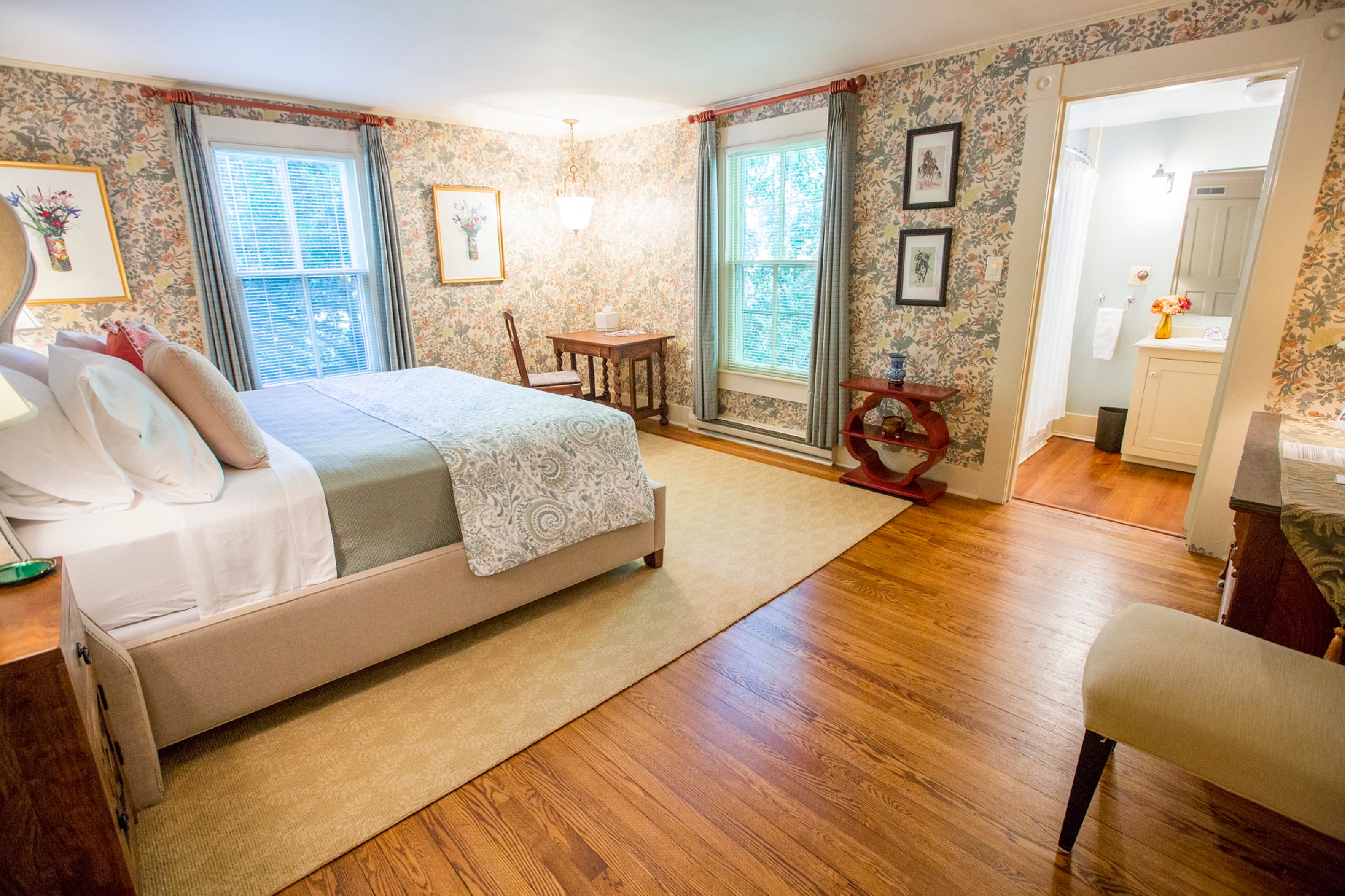 A cozy bedroom with floral wallpaper, a queen bed, and an adjoining bathroom.