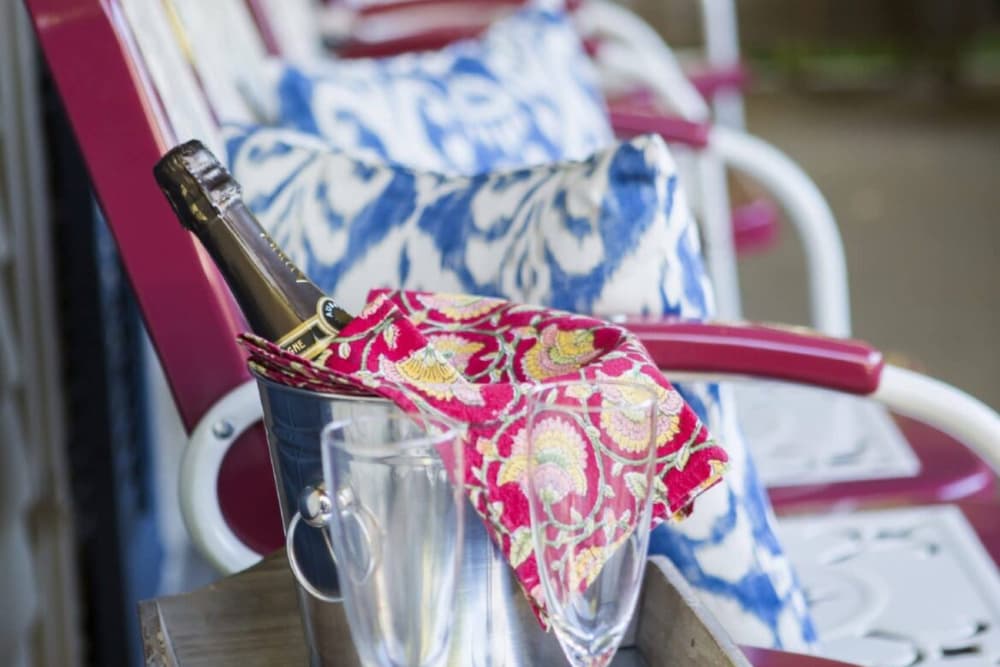 A wine bottle rests in a bucket with a decorative napkin, alongside two empty glasses on a table.