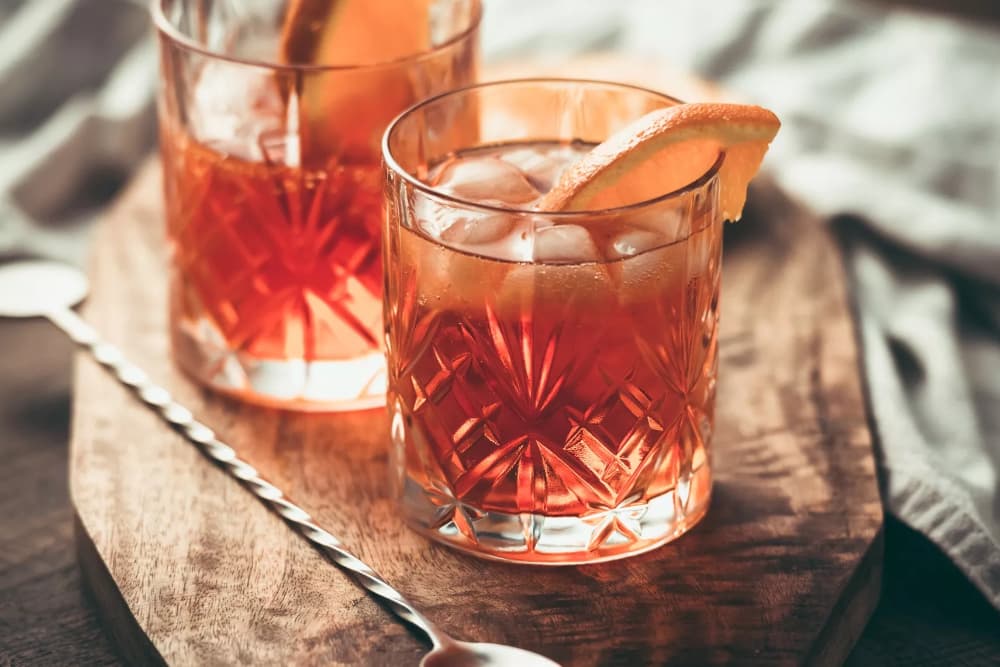 Two glasses of cocktail with orange slices on a wooden board.