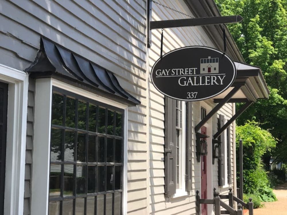A sign for the Gay Street Gallery hangs outside a building with a light gray exterior.