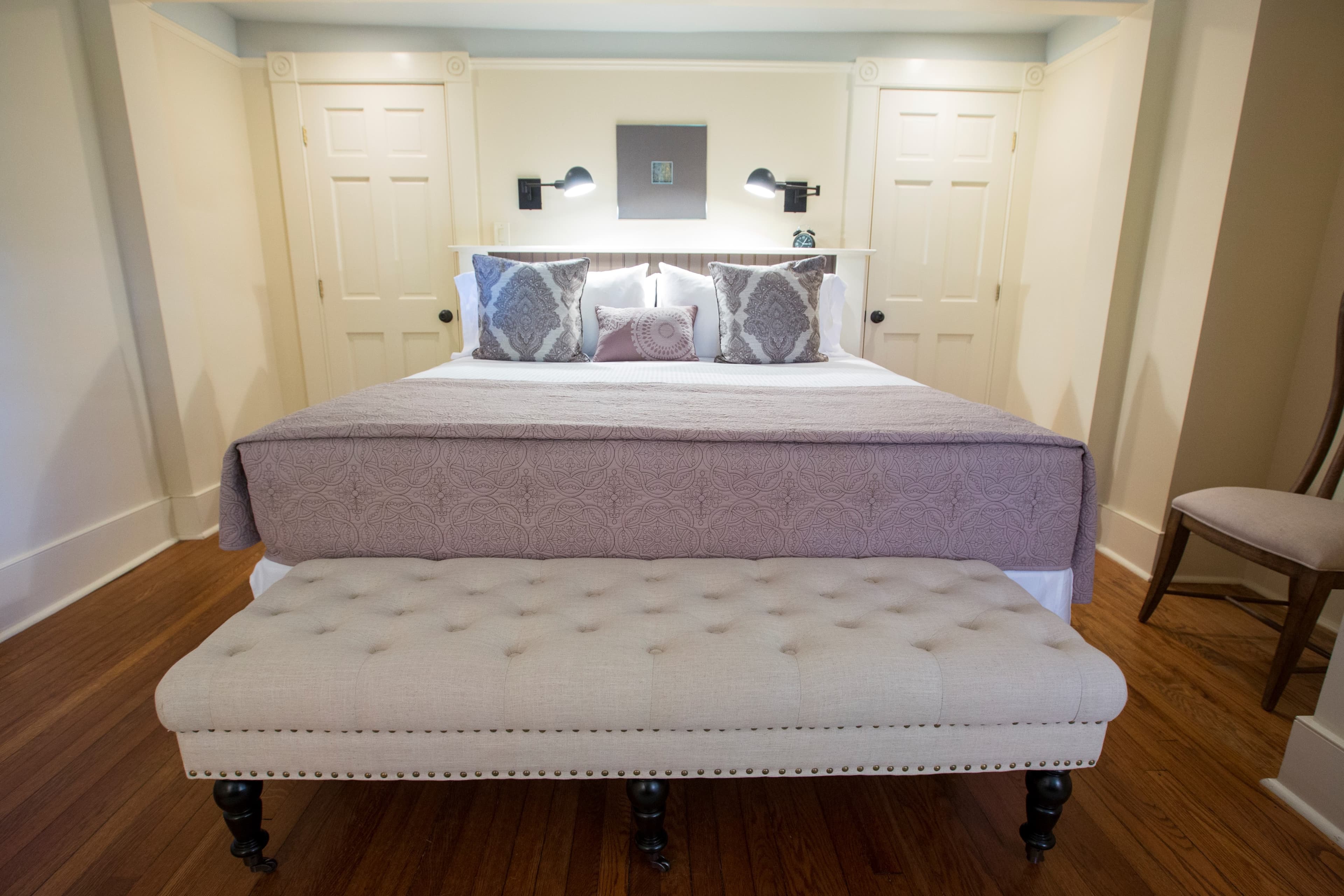 A cozy bedroom featuring a neatly made bed with decorative pillows and a upholstered bench at the foot.