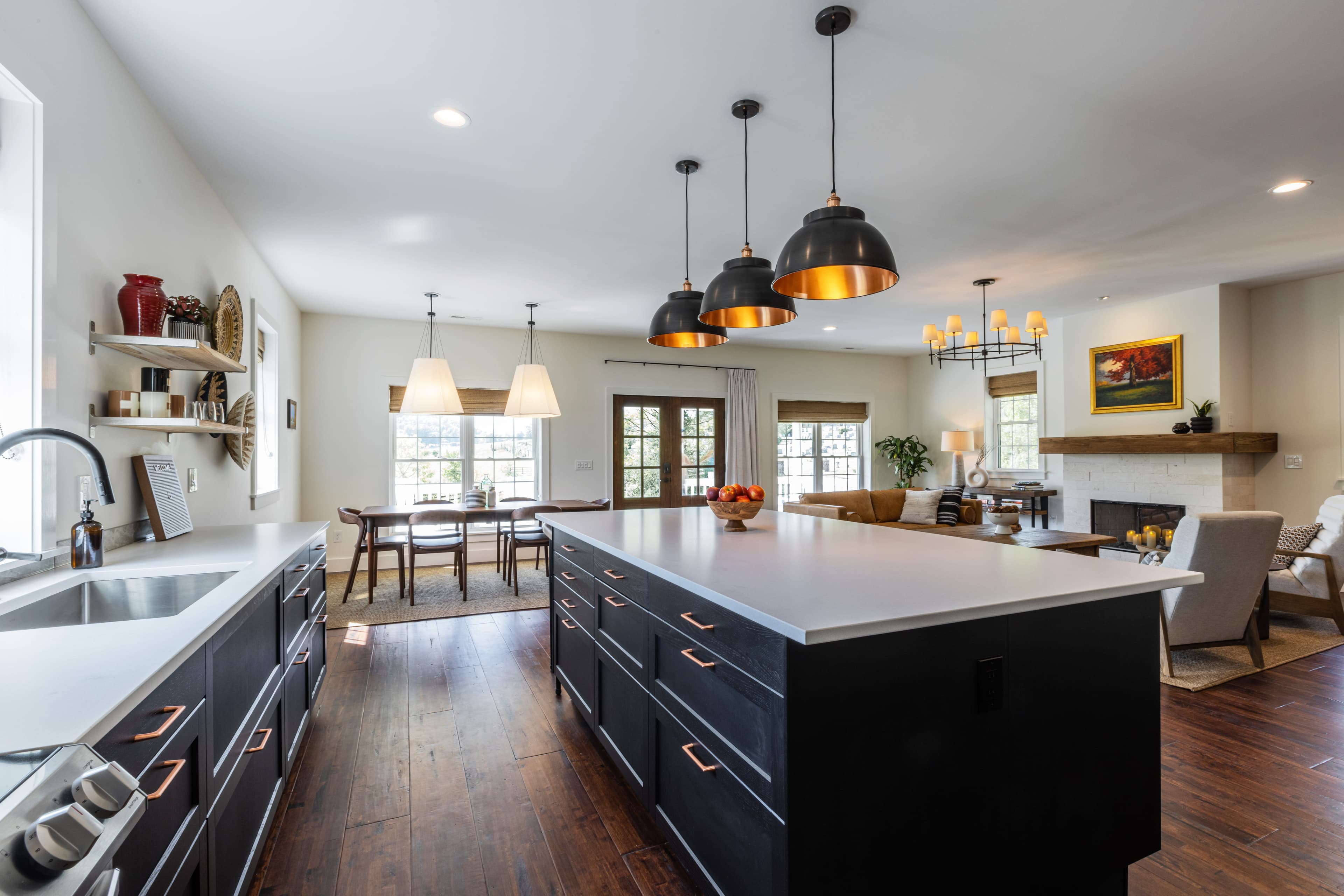 A modern kitchen featuring a large island, dark cabinetry, and pendant lighting, overlooking a bright dining area.
