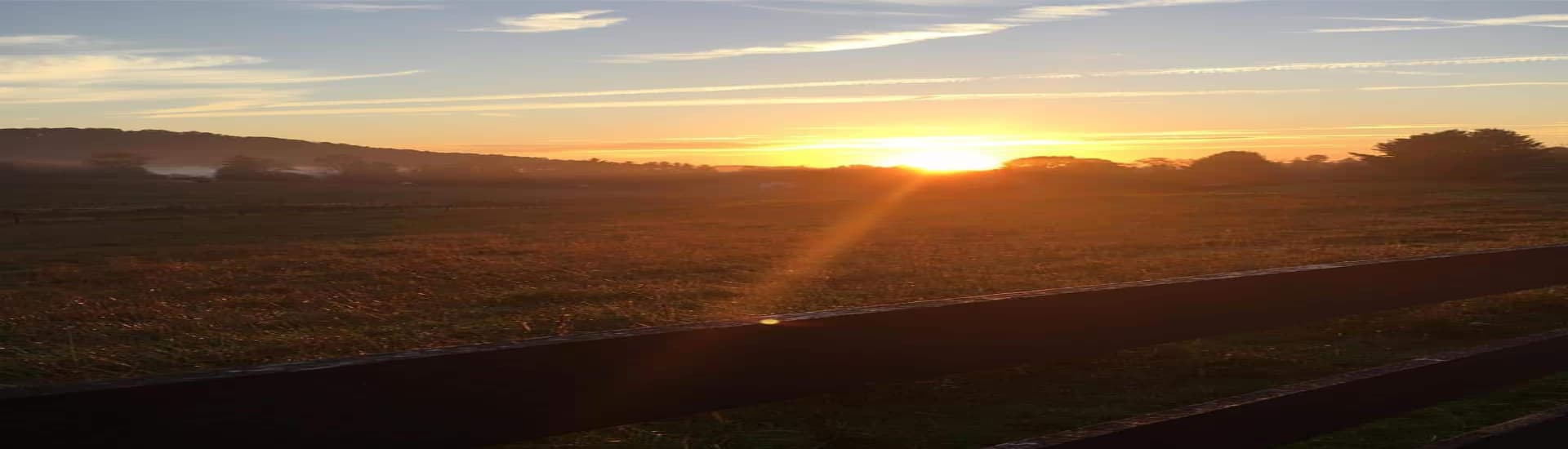 Sunrise over a field with a wooden fence in the foreground.