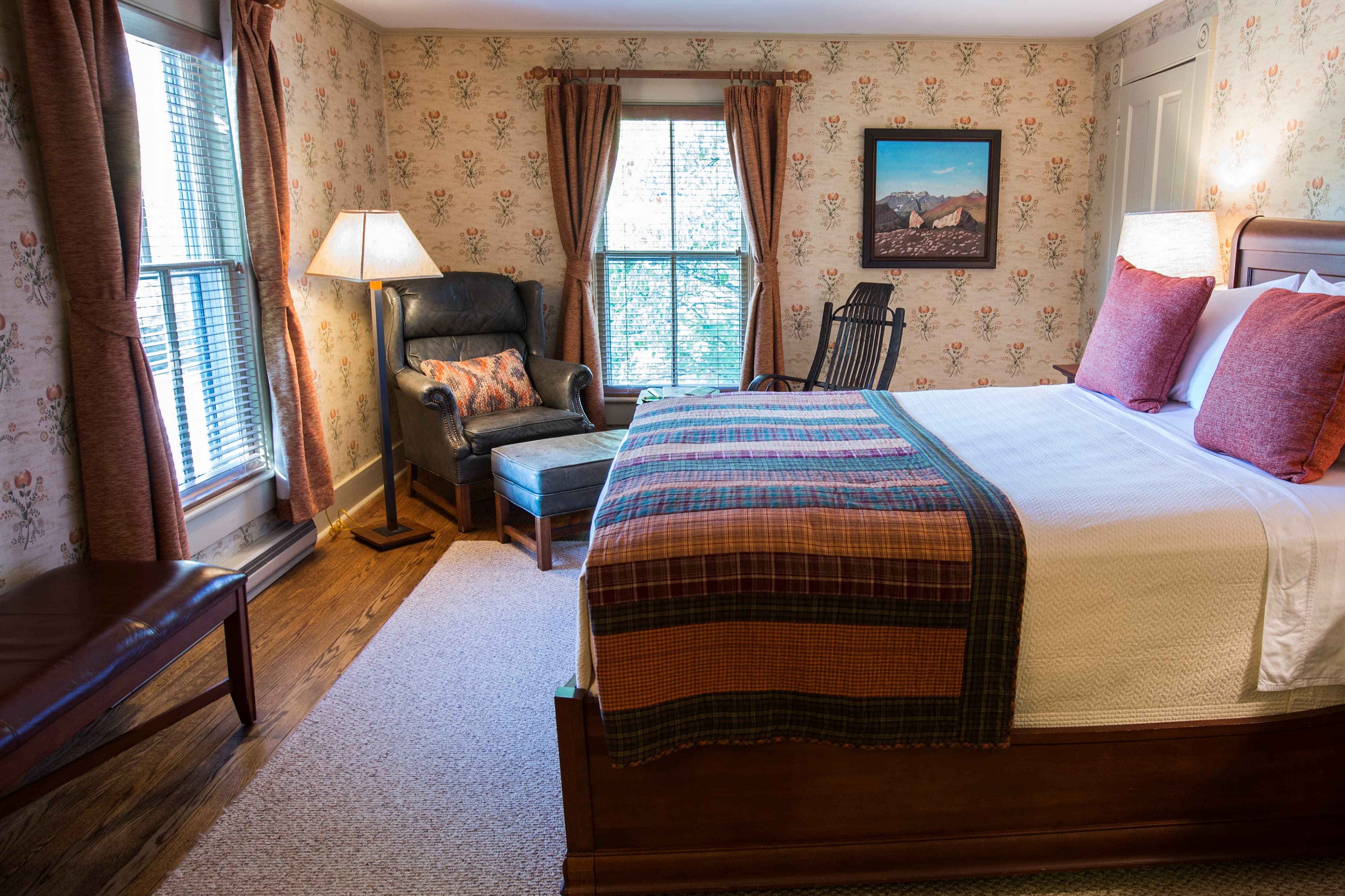 Cozy bedroom featuring a bed with a plaid blanket, an armchair, and patterned wallpaper.