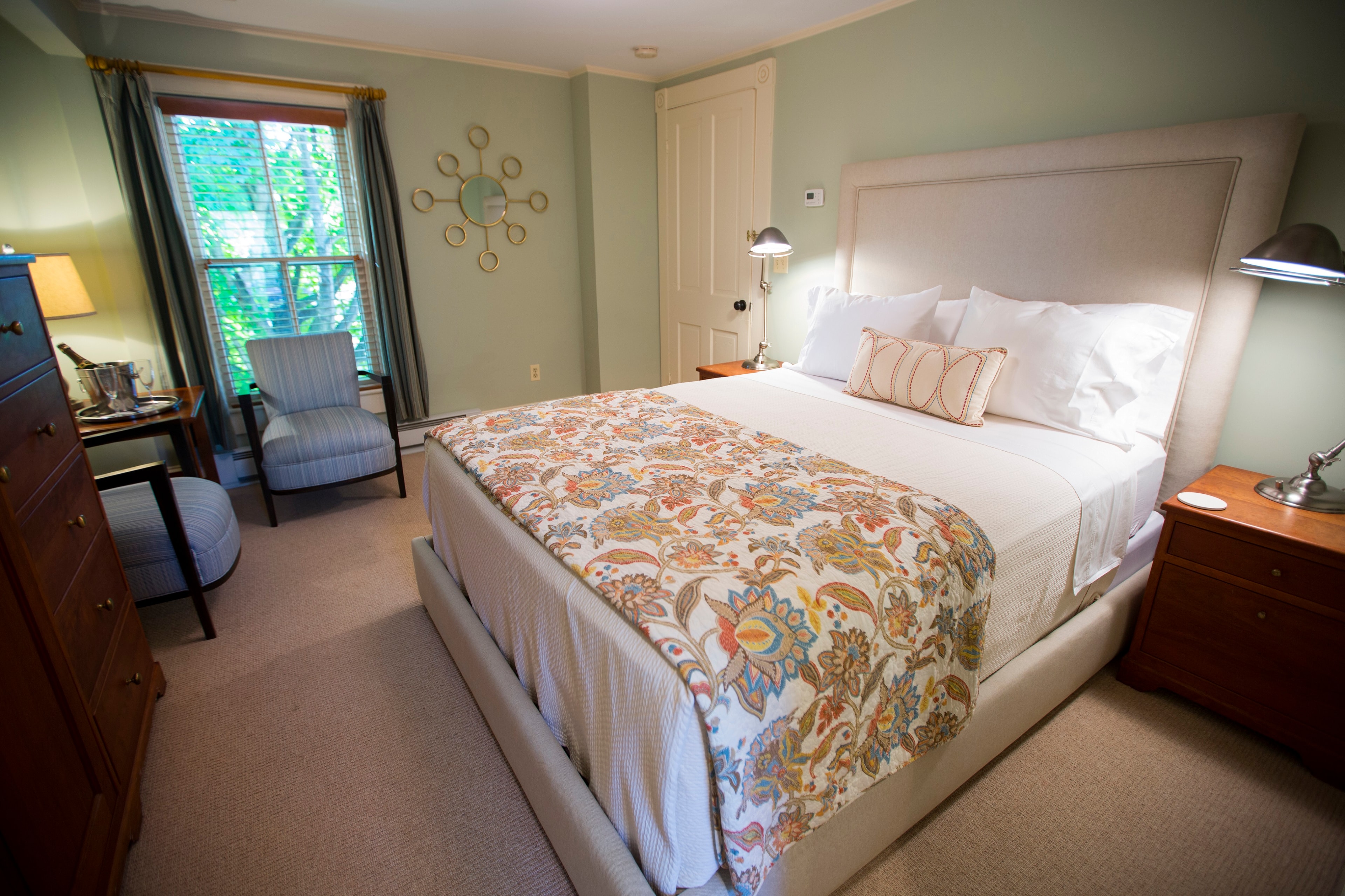 A cozy bedroom featuring a plush bed, patterned blanket, and a chair by the window.