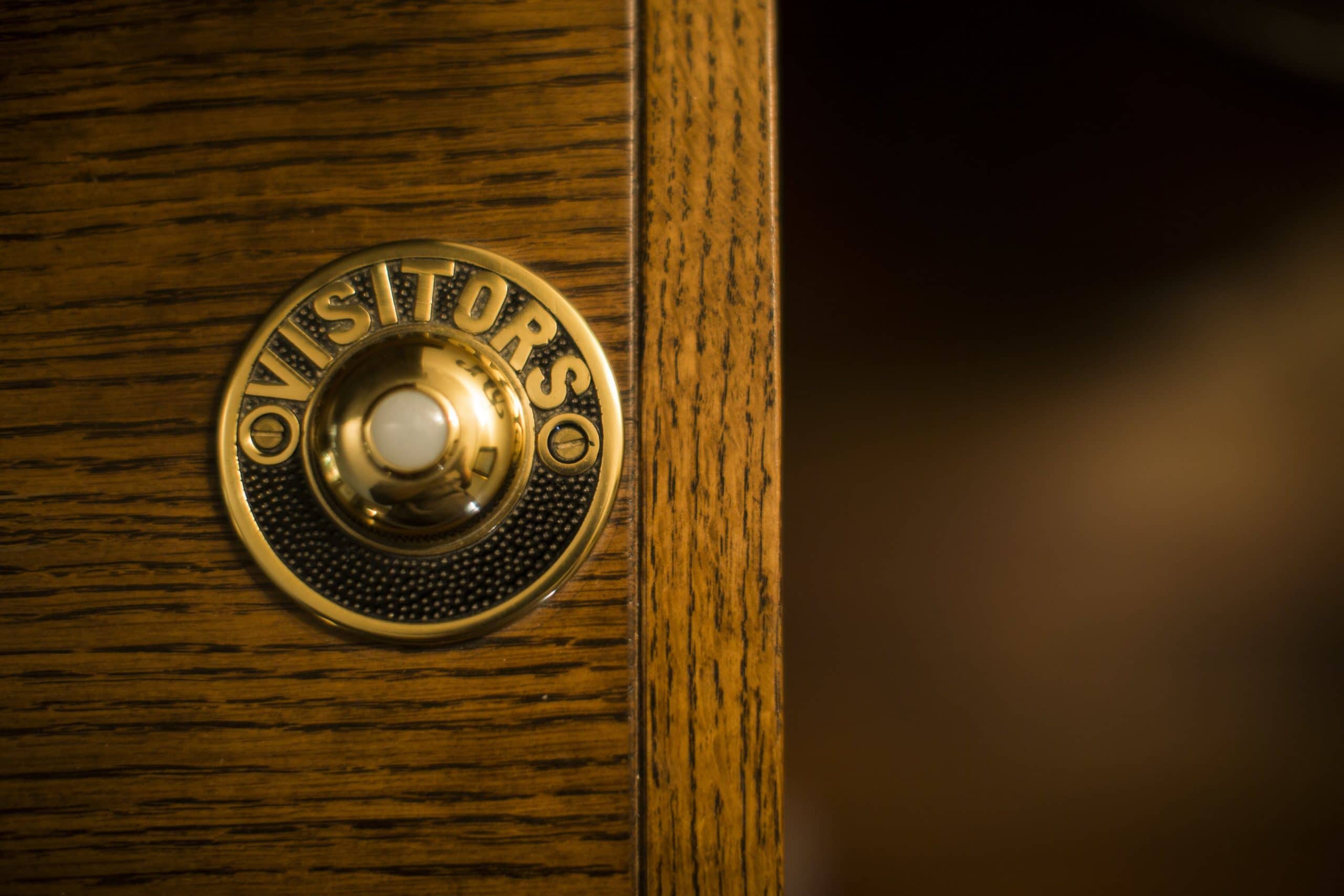 A brass doorbell that says Visitors on it.