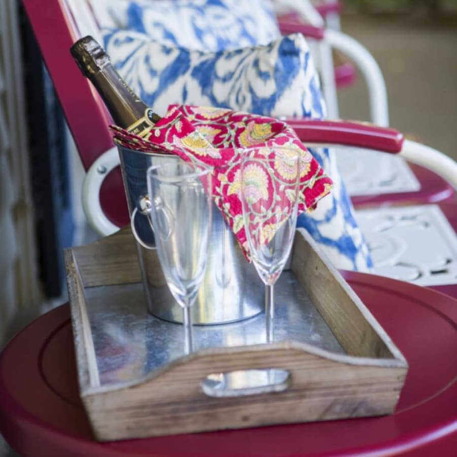 A silver ice bucket with a wine bottle and two champagne flutes on a rustic wooden tray.