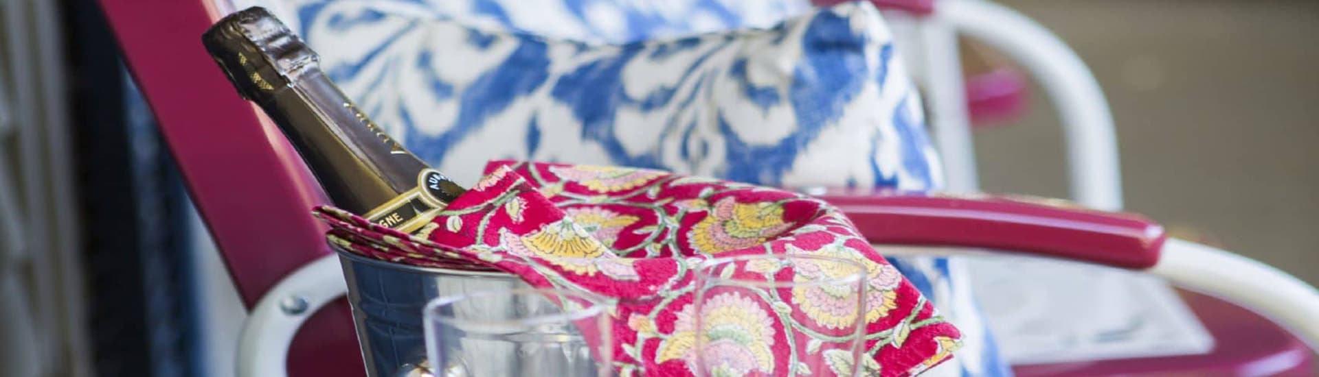 A bottle of champagne in an ice bucket with a colorful cloth on a lounge chair.