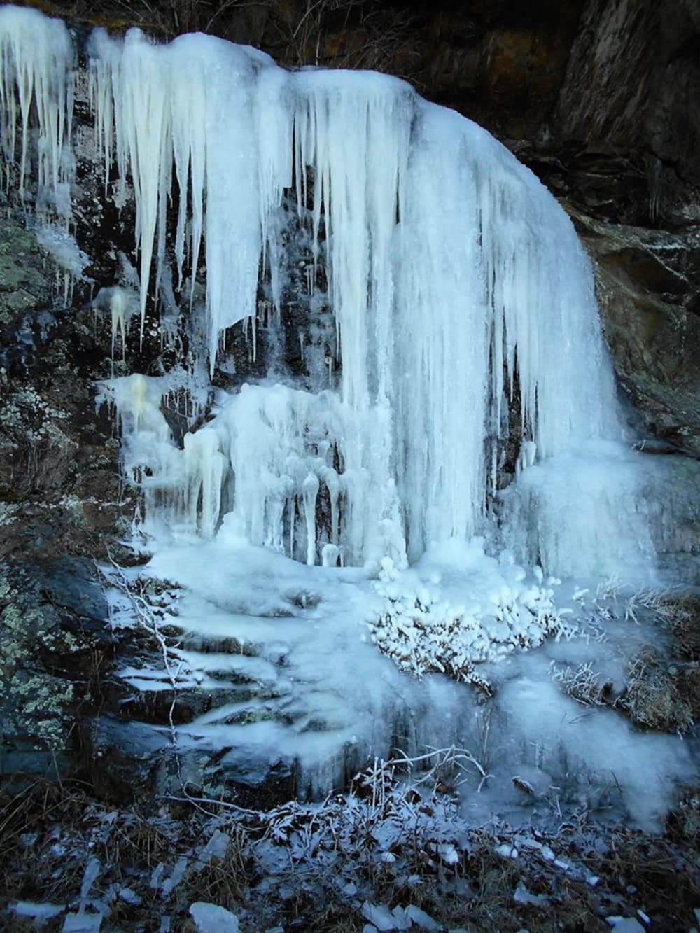 Icicles hang from a rocky cliff, surrounded by a frozen landscape.