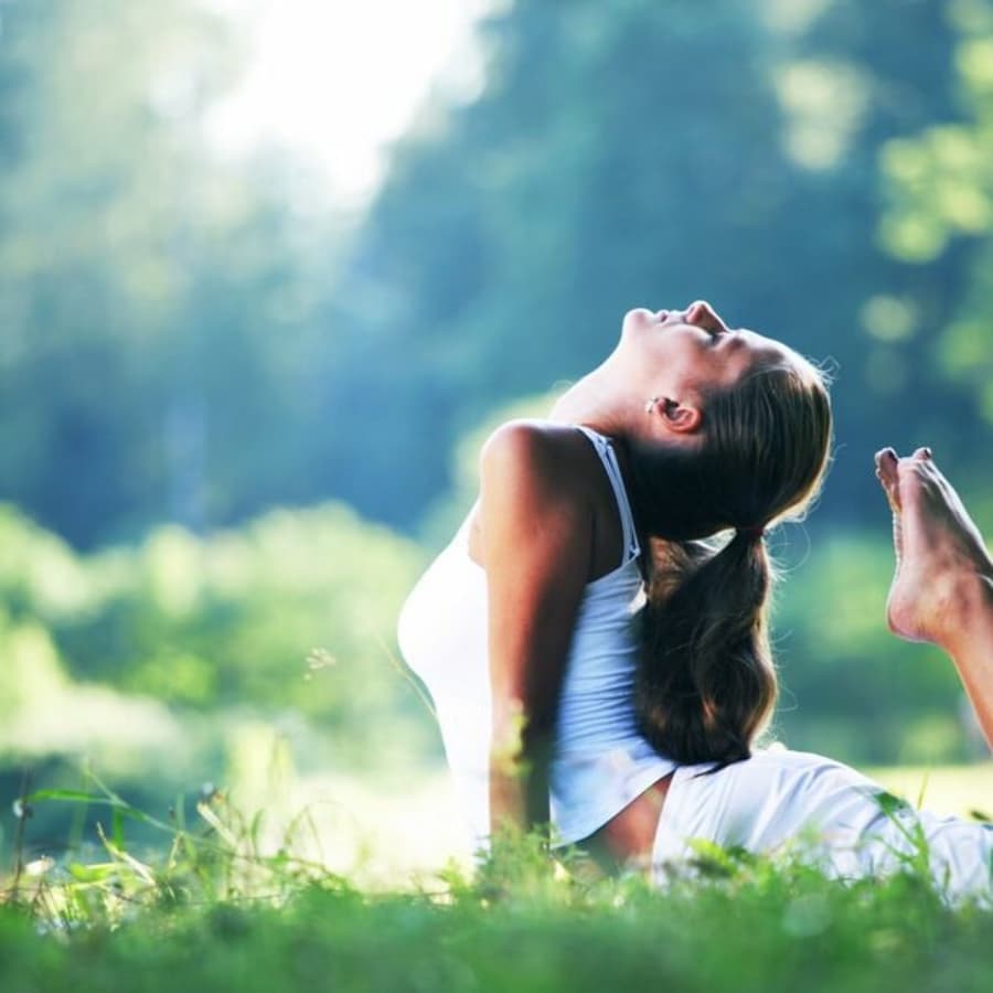 A woman practices yoga outdoors with a serene expression.