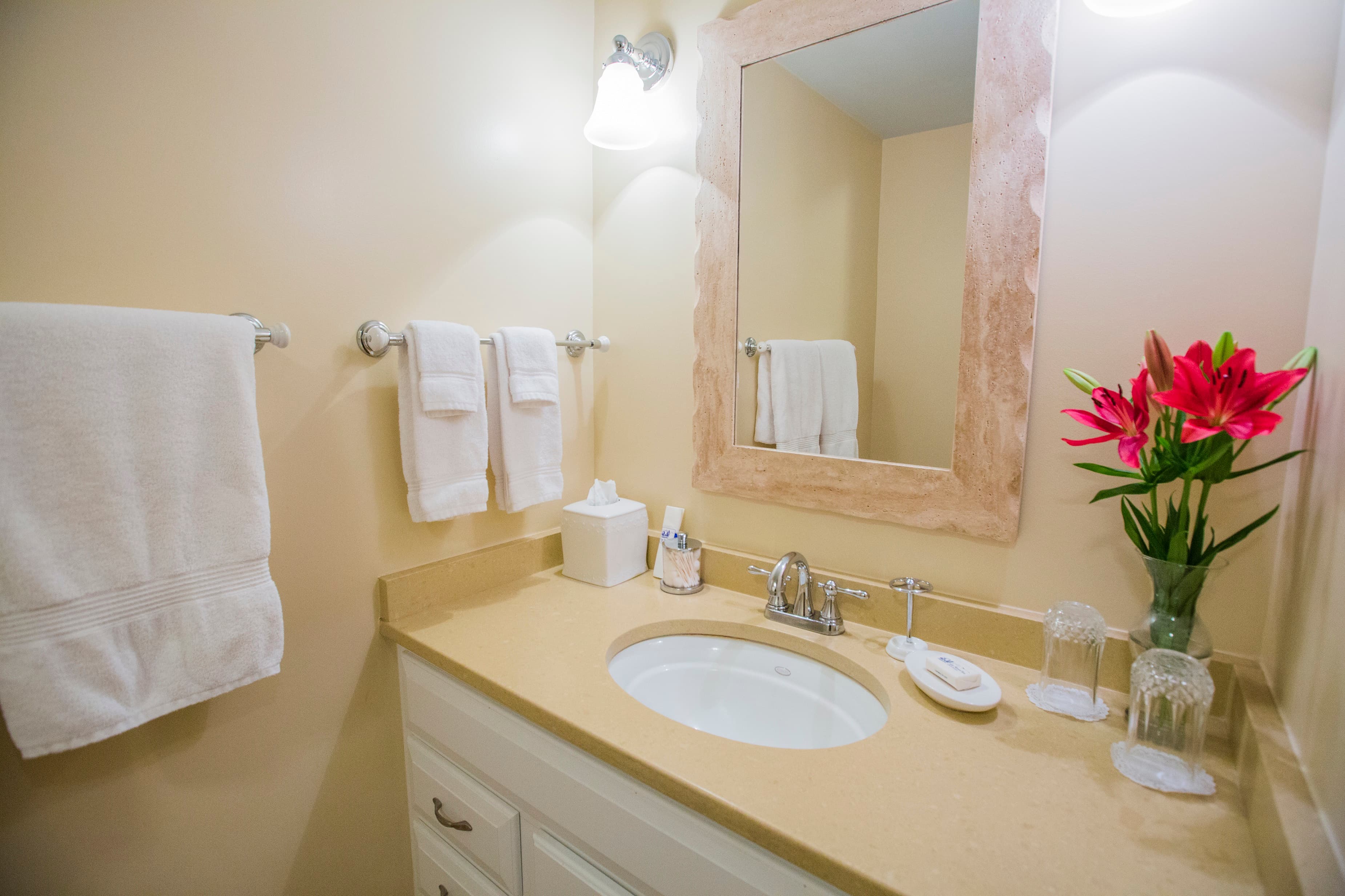 A clean bathroom with a sink, mirror, fresh towels, and a vase of flowers.