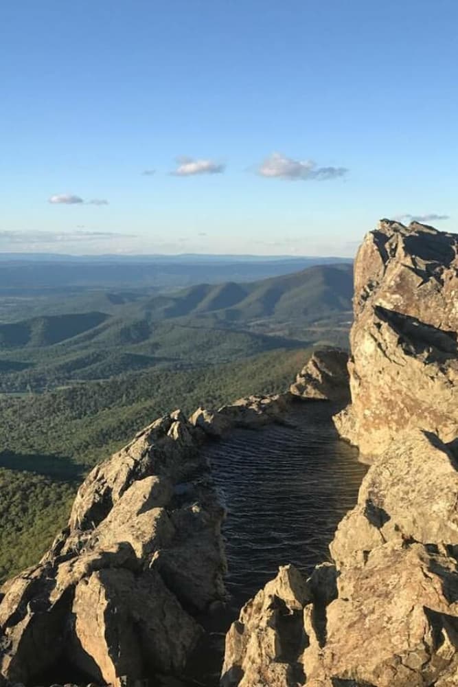 Panoramic view of mountains with a rocky outcrop and small pond in the foreground.