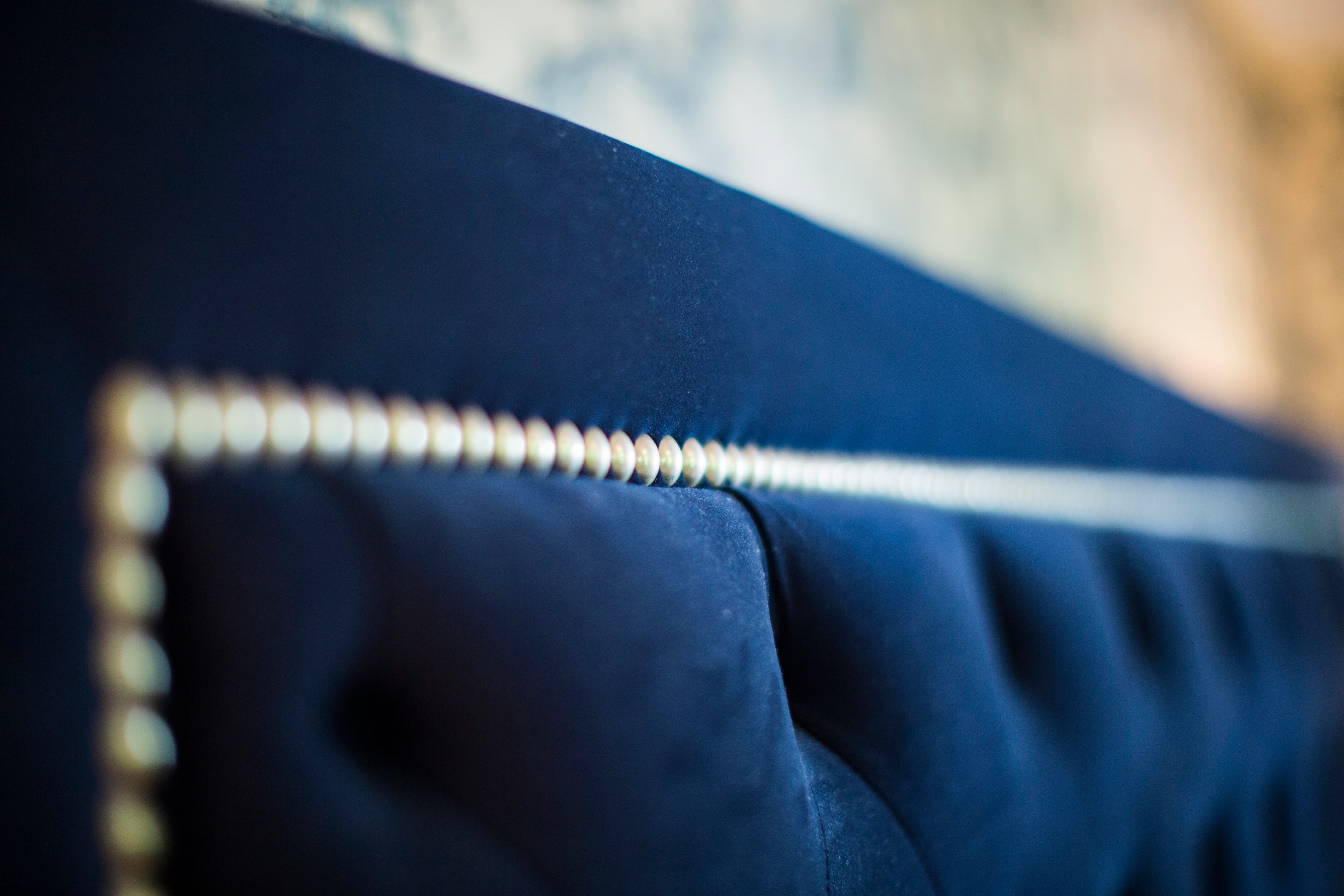 Close-up of a dark blue tufted upholstered headboard with decorative nailhead trim.